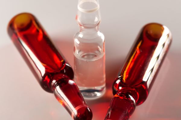 Glass ampoules, one clear and two red, on a pale surface